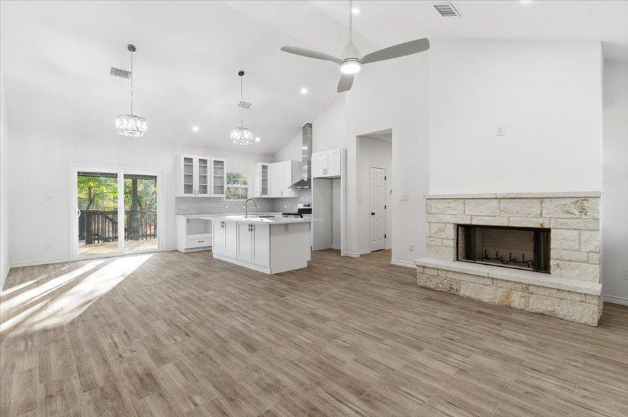 Unfurnished living room with high vaulted ceiling, a fireplace, ceiling fan, a chandelier, and light wood-style floors