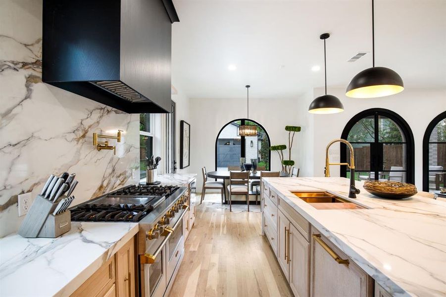 Gourmet kitchen featuring a built-in range, a striking marble-finish backsplash, and an expansive island with an undermount sink Gourmet kitchen featuring a built-in range, a striking marble-finish backsplash, and an expansive island with an undermount sink