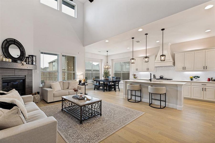Open-concept living space featuring high ceilings, wood-finish flooring, a fireplace with a wood mantle, a kitchen island with seating, and pendant lighting