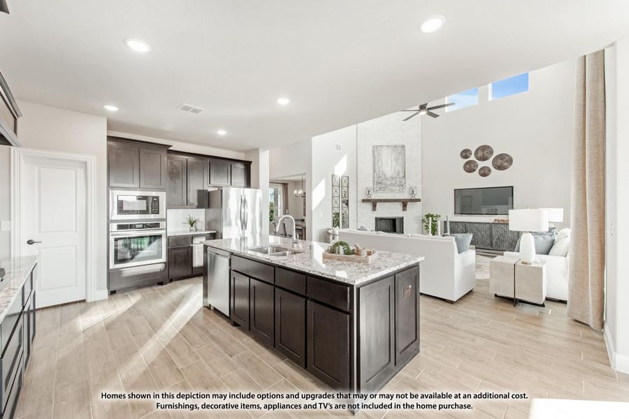 Open-concept kitchen with dark cabinets, granite island, and living room with fireplace visible beyond Open-concept kitchen with dark cabinets, granite island, and living room with fireplace visible beyond