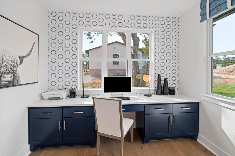 Office space featuring light wood-type flooring, an accent wall, and wallpapered walls. The photos shown are of a completed home with the same floor plan and may not reflect the exact finishes, features, or layout of the home currently under construction.