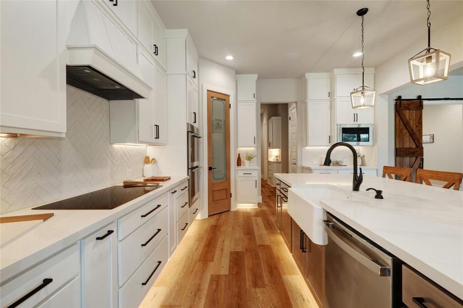 Modern kitchen featuring white cabinetry, quartz countertops, a herringbone tile backsplash, stainless steel appliances, and wood-finish flooring