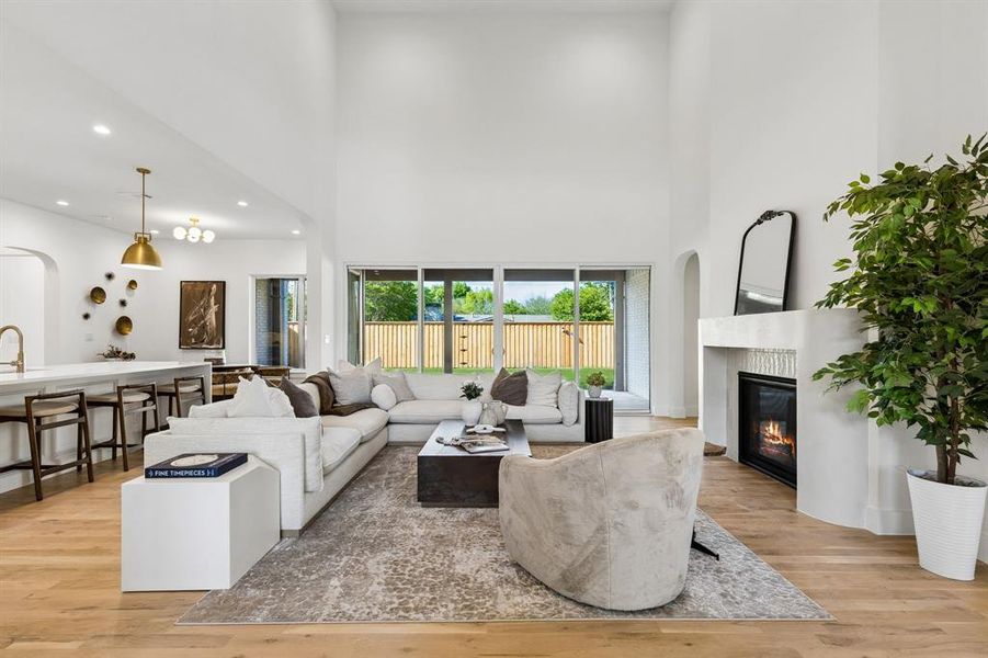 Living area with arched walkways, light wood finished floors, a glass covered fireplace, recessed lighting, and a high ceiling
