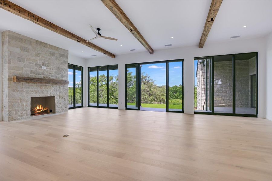 A spacious living area with exposed beam ceilings and a stone fireplace, offering panoramic views of lush greenery.