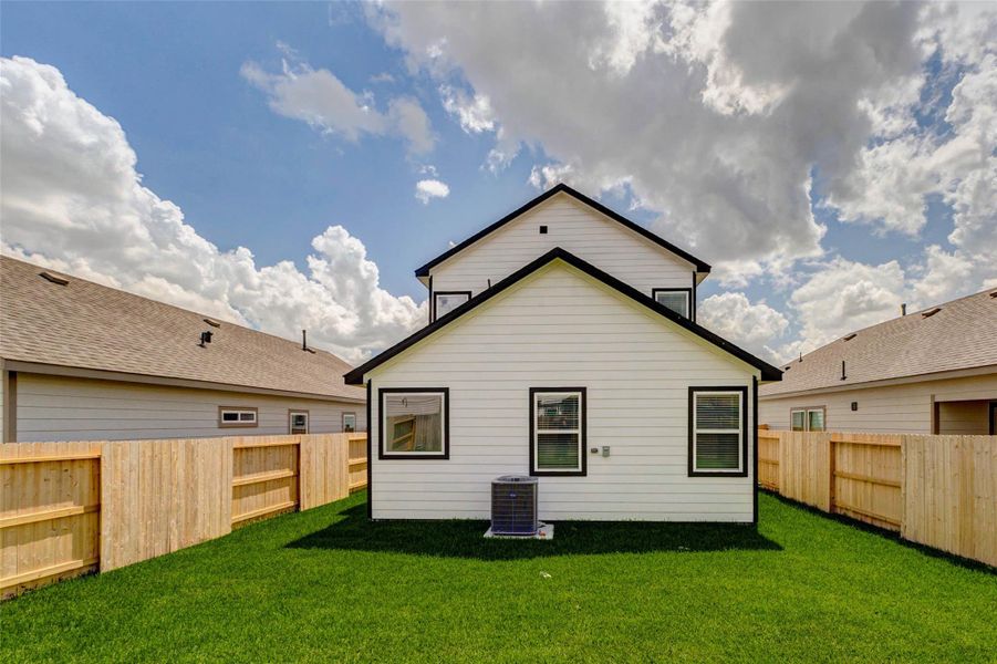 Straight-on rear exterior view highlighting the fenced backyard, fresh lawn, rear windows, and private outdoor setting. The full wood fencing creates a defined backyard space, while the simple rear elevation provides a clean backdrop for future patio furniture or outdoor living.