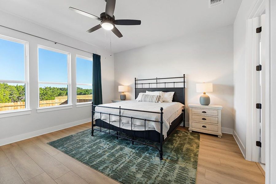 Sunlight streams through large windows onto smooth wood flooring in this serene bedroom.