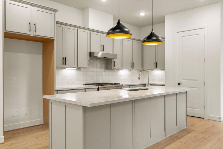 Gourmet workspace layout — sleek gooseneck faucet, warm light-wood flooring, and custom cabinetry with dedicated refrigerator alcove.