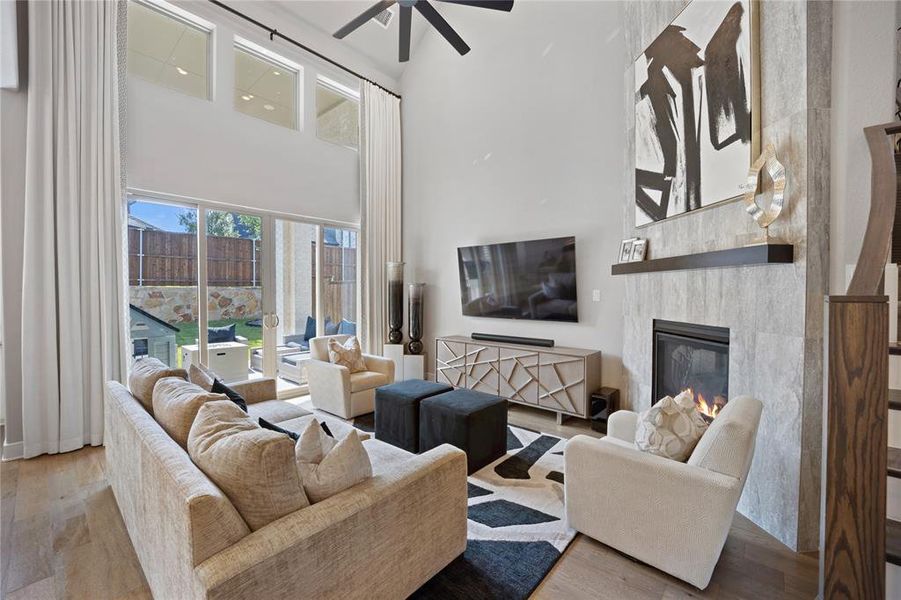 Living room with a towering ceiling, light hardwood / wood-style flooring, a tiled fireplace, and ceiling fan