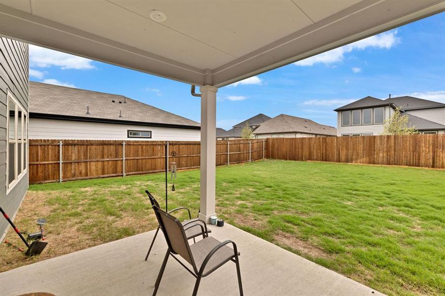 The property features a concrete patio with an overhead cover, overlooking a fenced backyard with a lawn