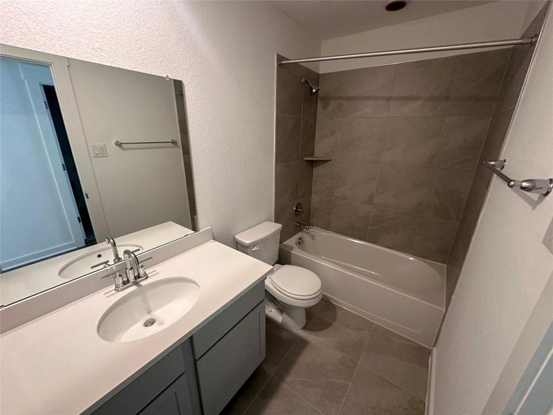 Bathroom featuring a textured wall, shower / tub combination, vanity, and dark tile patterned floors Bathroom featuring a textured wall, shower / tub combination, vanity, and dark tile patterned floors