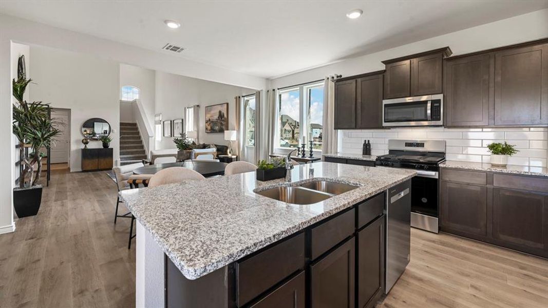 Kitchen featuring stainless steel appliances, dark brown cabinetry, open floor plan, backsplash, and light wood-style flooring Kitchen featuring stainless steel appliances, dark brown cabinetry, open floor plan, backsplash, and light wood-style flooring