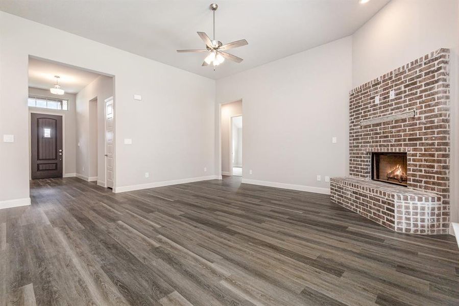 Unfurnished living room featuring dark wood finished floors, a ceiling fan, and a brick fireplace Unfurnished living room featuring dark wood finished floors, a ceiling fan, and a brick fireplace
