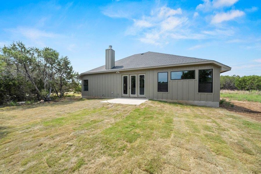 Rear view of property with board and batten siding, a chimney, french doors, a patio area, and a yard Rear view of property with board and batten siding, a chimney, french doors, a patio area, and a yard