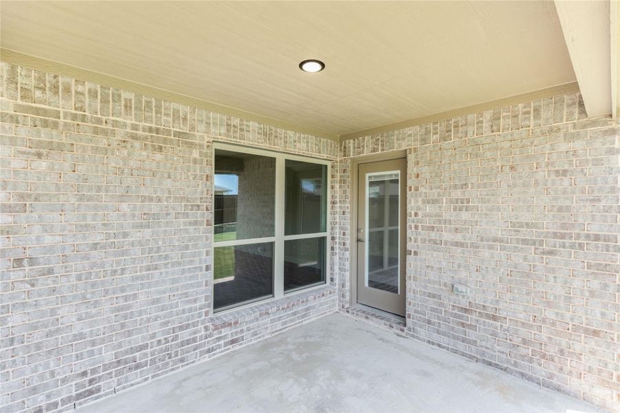 Covered back patio with light brick walls, glass door, and large window with concrete floor Covered back patio with light brick walls, glass door, and large window with concrete floor