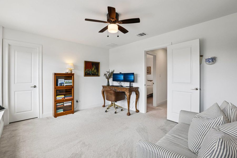 This room features white walls, light-colored carpeting, and a dark wood ceiling fan with an integrated light fixture