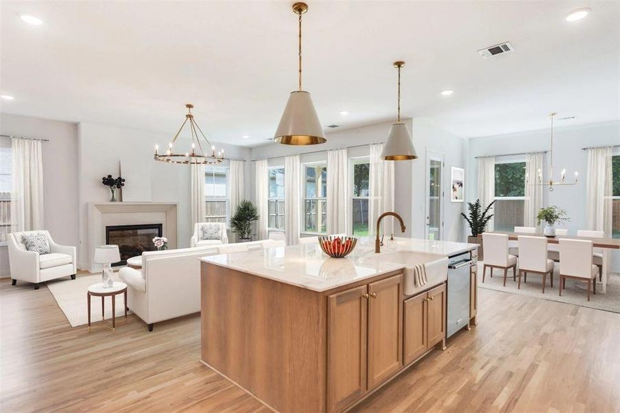 Kitchen with a chandelier, light wood-style flooring, a glass covered fireplace, a center island with sink, and recessed lighting