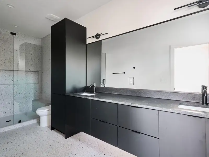 Bathroom featuring double vanity, a walk in shower, and dark aggregate flooring Bathroom featuring double vanity, a walk in shower, and dark aggregate flooring