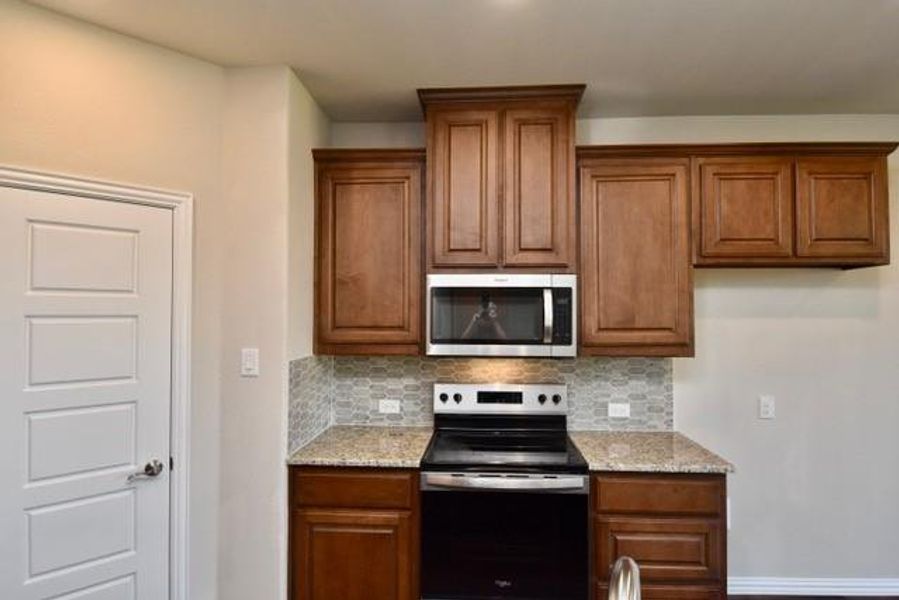 Kitchen featuring appliances with stainless steel finishes, brown cabinetry, light stone counters, and tasteful backsplash Kitchen featuring appliances with stainless steel finishes, brown cabinetry, light stone counters, and tasteful backsplash