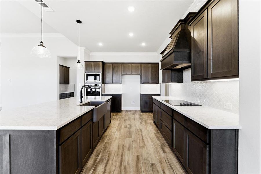 Kitchen featuring light stone counters, a large island, decorative light fixtures, light wood-style flooring, and dark brown cabinets