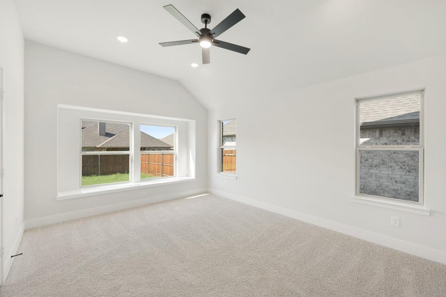 Empty bedroom with vaulted ceiling, ceiling fan, carpet flooring, and multiple windows Empty bedroom with vaulted ceiling, ceiling fan, carpet flooring, and multiple windows