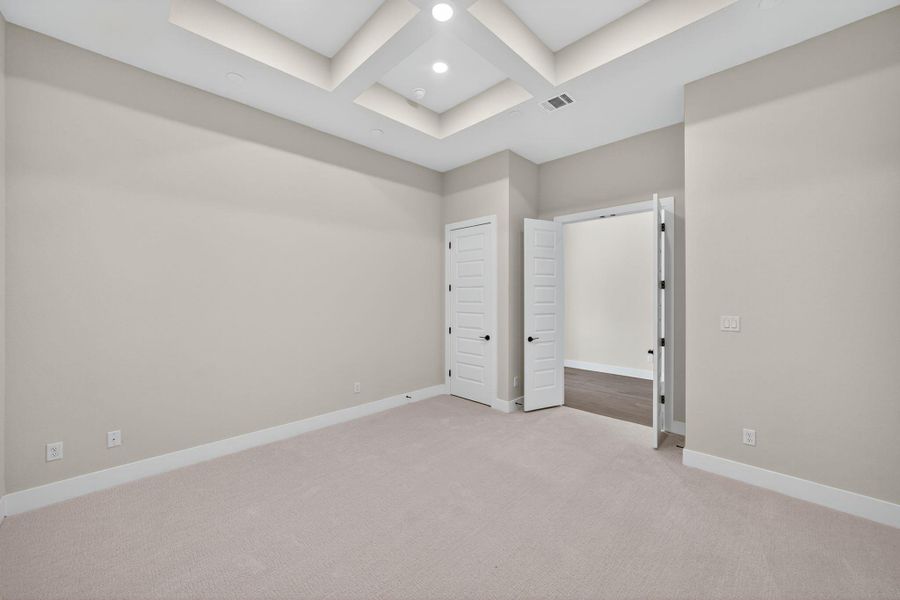 Unfurnished bedroom featuring coffered ceiling, light colored carpet, and beamed ceiling Unfurnished bedroom featuring coffered ceiling, light colored carpet, and beamed ceiling