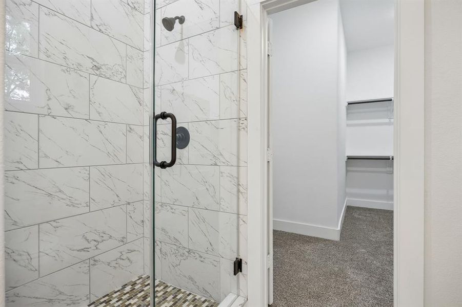 Glass-enclosed shower with white marble-style tile walls and mosaic-tiled shower pan