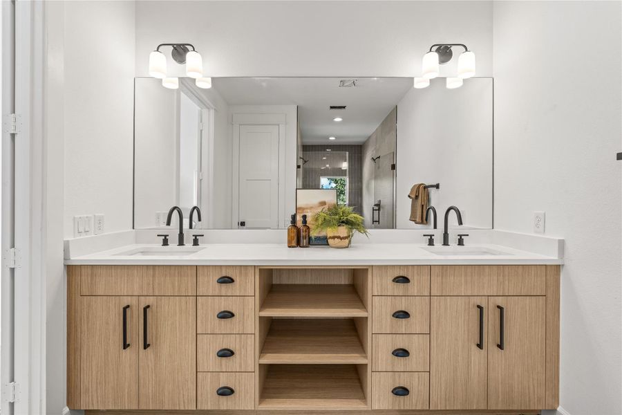 Straight-on view of the primary en-suite bathroom's expansive double vanity with light wood cabinetry, open shelving, and black hardware. Straight-on view of the primary en-suite bathroom's expansive double vanity with light wood cabinetry, open shelving, and black hardware.