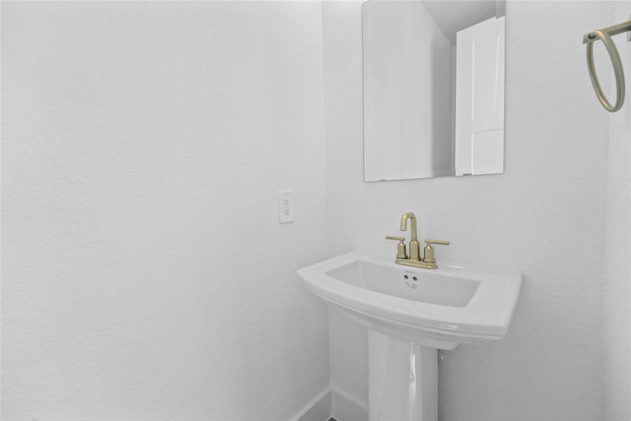 The first-floor powder room offers convenience and a modern aesthetic. It features a classic white pedestal sink complemented by a sleek faucet and a matching wall-mounted towel ring. A simple, large rectangular mirror enhances the sense of space and reflects the bright white walls, making this half-bath both functional and stylish.