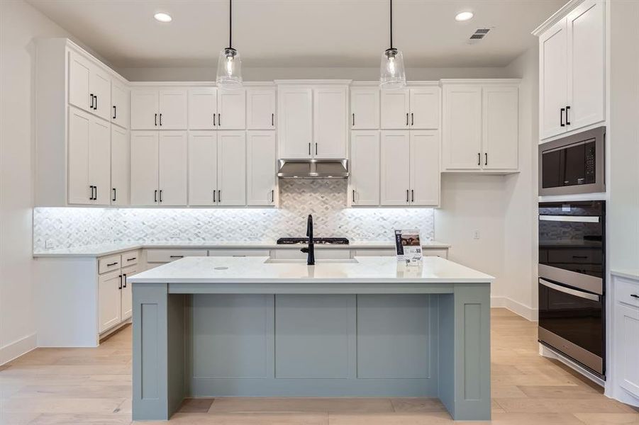 Kitchen with decorative light fixtures, a center island with sink, and white cabinets