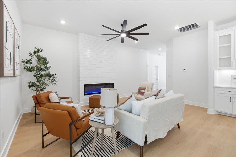 Living room featuring light wood-style floors, a large fireplace, ceiling fan, and recessed lighting