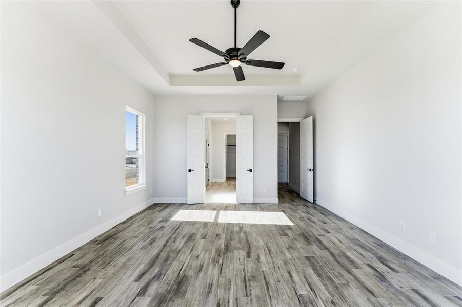 Unfurnished bedroom with a raised ceiling, wood finished floors, a ceiling fan, and a walk in closet
