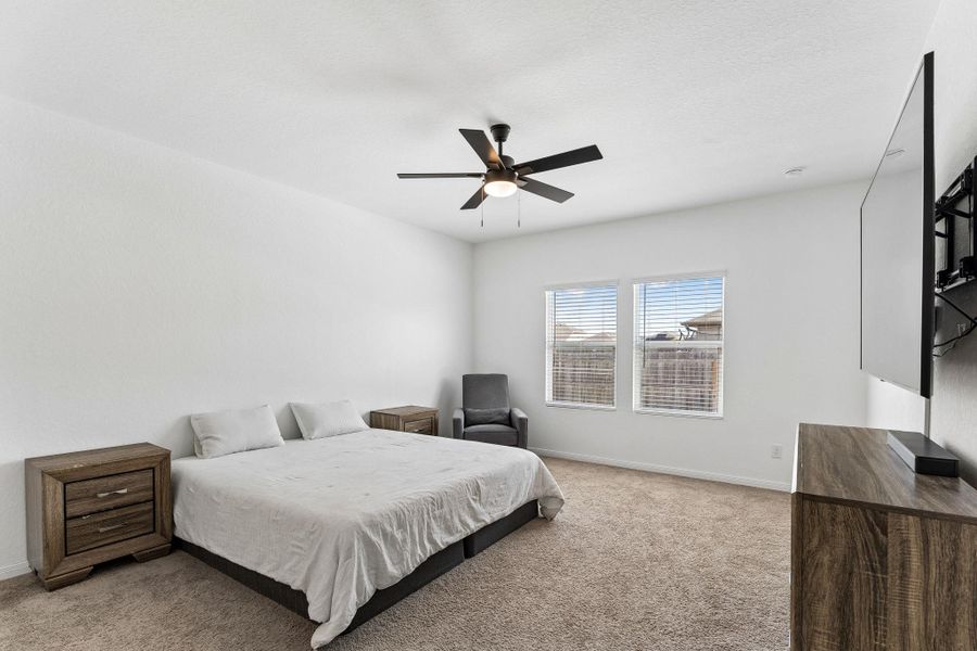 Well-lit primary bedroom  with clean carpet and bright, clear windows.