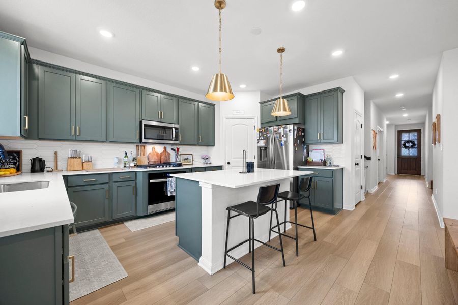 Modern kitchen featuring a central island with countertop seating, stainless steel appliances, recessed lighting, and wood-finish flooring
