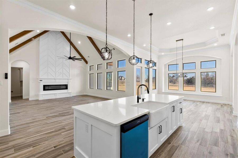 Kitchen with a fireplace, dishwasher, hanging light fixtures, white cabinets, and an island with sink