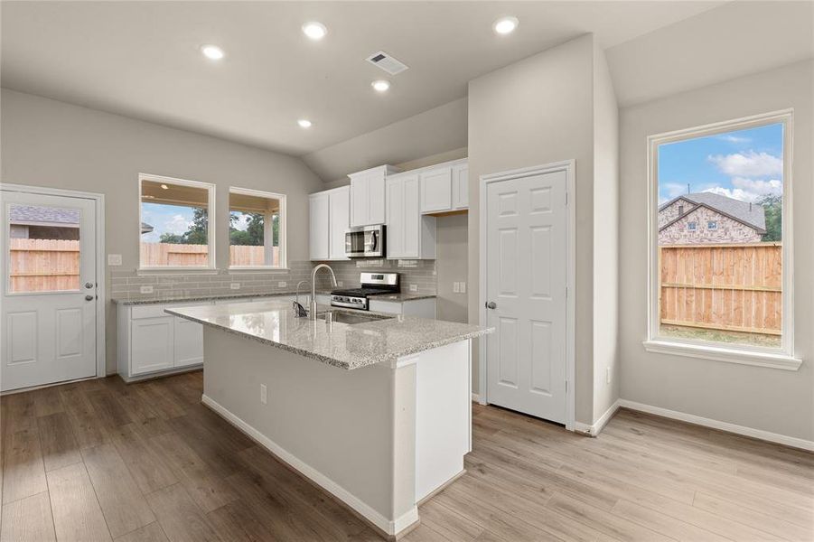 This light and bright kitchen features a large quartz island, white cabinets, a large sink overlooking your family room, recessed lighting, and beautiful backsplash.