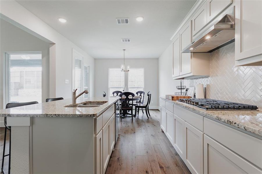 Modern kitchen featuring light cabinetry, a gas cooktop with an overhead range hood, and a herringbone-patterned tile backsplash