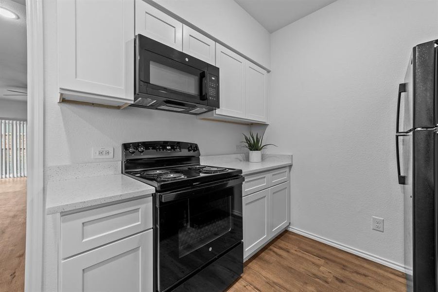 Kitchen with white cabinetry, black appliances, dark hardwood / wood-style flooring, and light stone counters