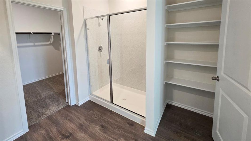Full bathroom featuring a spacious closet, dark wood-style flooring, and a stall shower Full bathroom featuring a spacious closet, dark wood-style flooring, and a stall shower