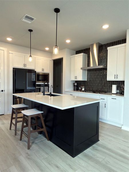 Modern kitchen featuring a large black island with a light-toned countertop, flanked by two pendant lights