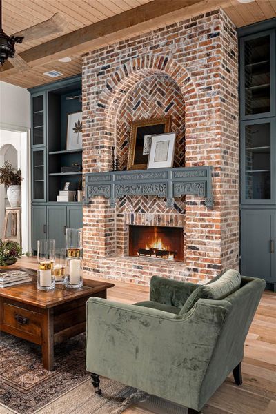 Living area featuring a wood ceiling with exposed beams, built in shelves, a fireplace, and wood finished floors