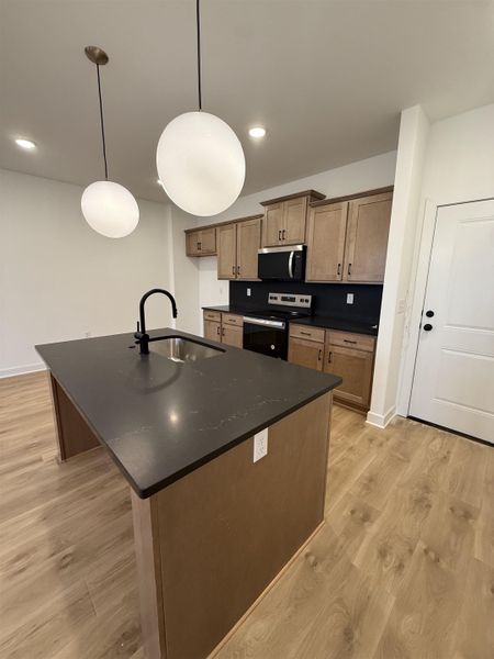 Kitchen featuring range with electric stovetop, light wood-type flooring, a center island with sink, and stainless steel microwave