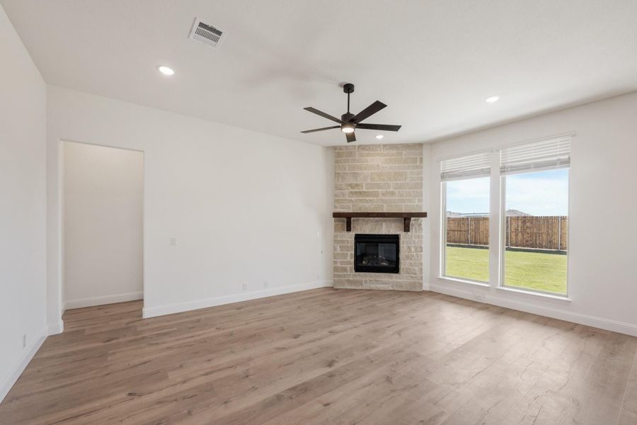 Open living room with stone fireplace, hardwood floors, ceiling fan, and large windows overlooking backyard Open living room with stone fireplace, hardwood floors, ceiling fan, and large windows overlooking backyard