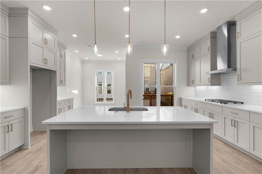 Kitchen with tasteful backsplash, hanging light fixtures, ornamental molding, light wood-style floors, and light stone counters