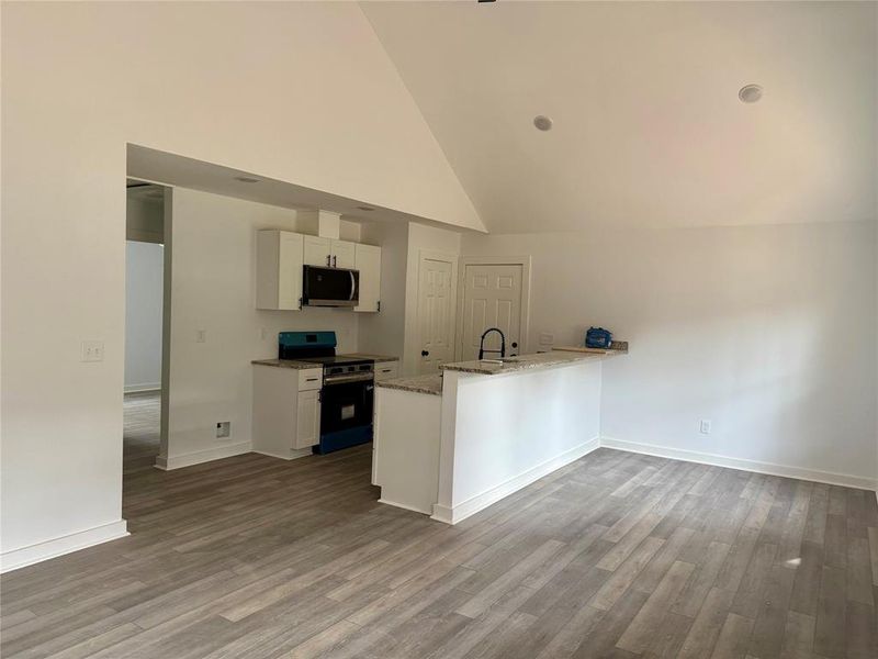 Kitchen featuring white cabinets, appliances with stainless steel finishes, light stone counters, high vaulted ceiling, and a peninsula