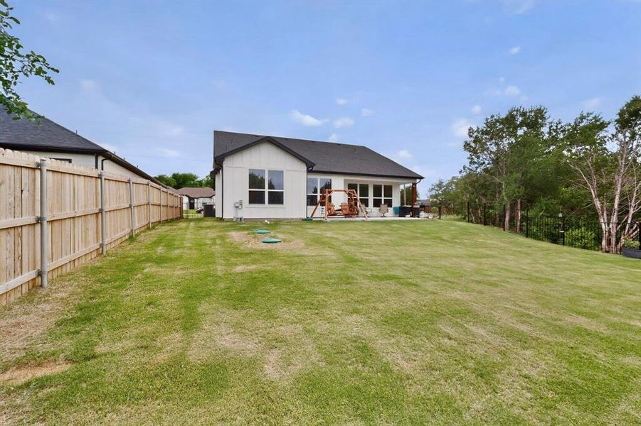 Expansive rear yard featuring a large grassy area, wood privacy fencing, and a treed border