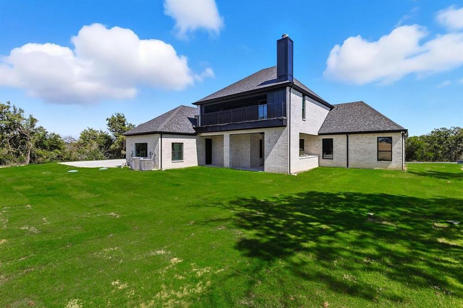 Rear view of property featuring a lawn, a balcony, and brick siding