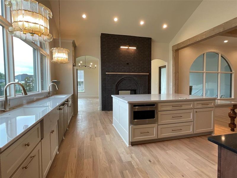 Kitchen featuring white cabinets, hanging light fixtures, a brick fireplace, a notable chandelier, and vaulted ceiling