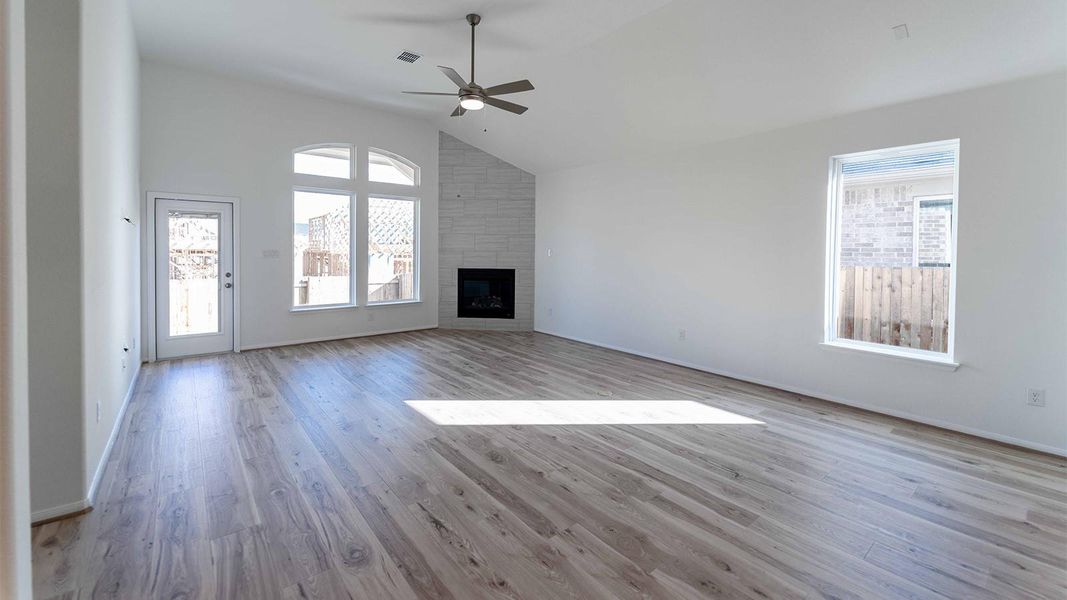 Unfurnished living room with vaulted ceiling, light wood-type flooring, a large fireplace, and a ceiling fan