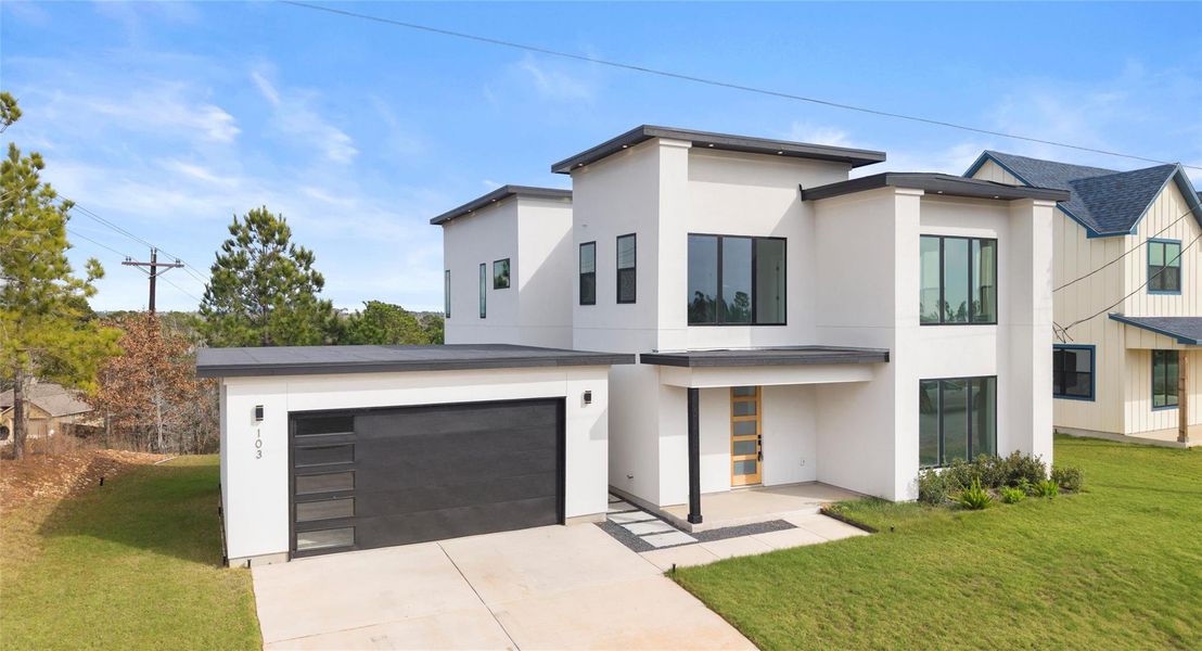 Contemporary house with a front yard, a garage, stucco siding, and driveway