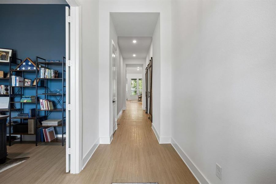 Bright hallway with wood-finish flooring, recessed lighting, and white baseboards Bright hallway with wood-finish flooring, recessed lighting, and white baseboards